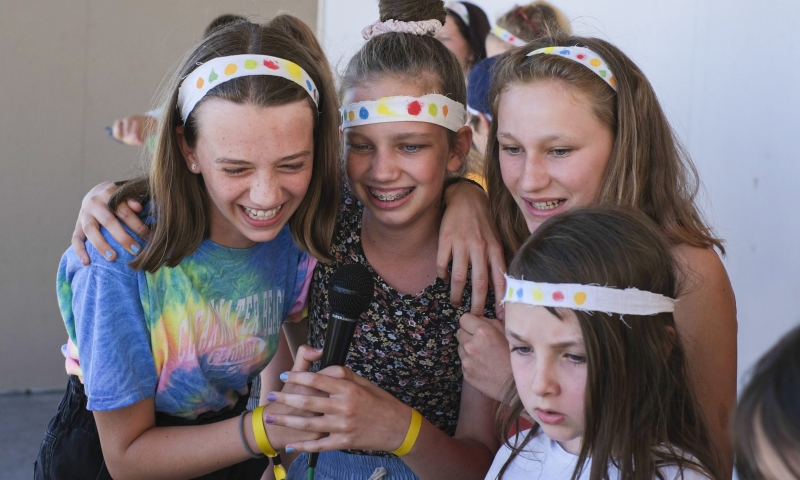 vier umarmende Mädchen singen erfreut Karaoke in ein Mikrofon