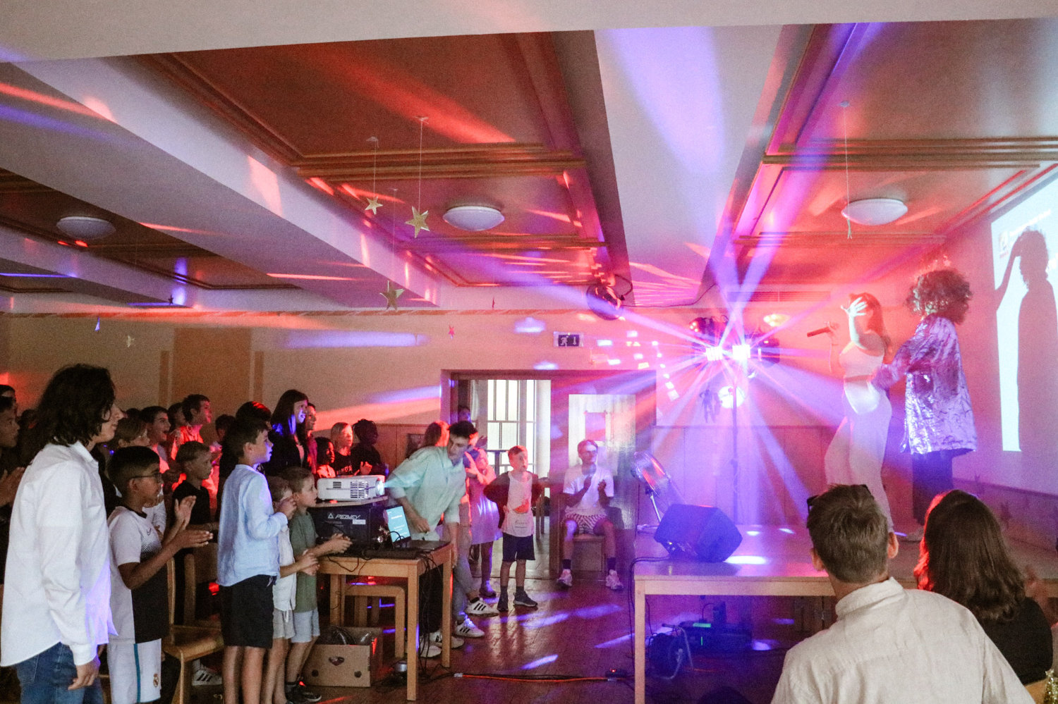 Vor der Bühne im Saal des Jugendgästehaus tanzen Kinder zur Musik. Der Saal ist ausgeleuchtet mit bunten Lichtern.